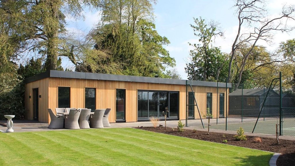 A timber-clad garden room with large sliding glass doors in a landscaped garden