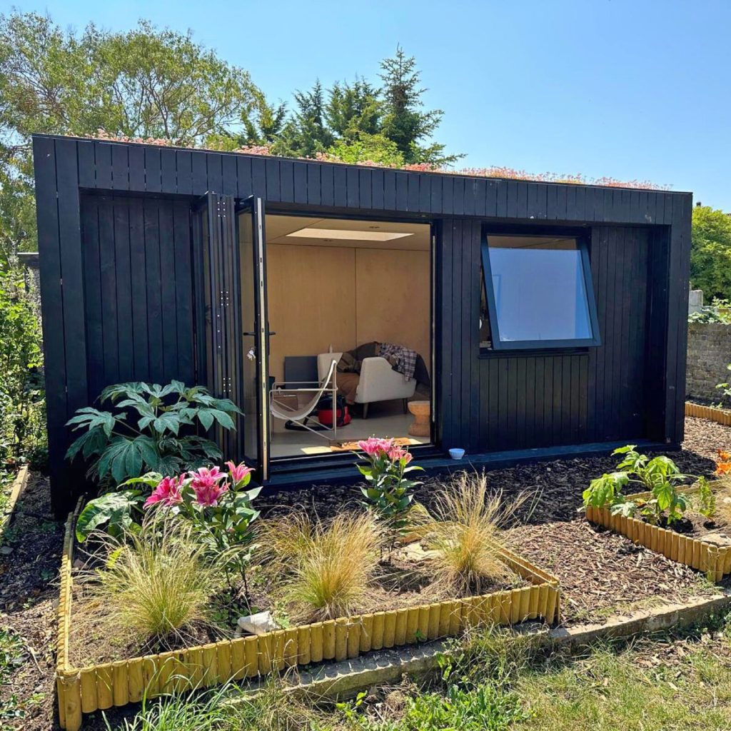 Black timber-clad garden room with bifold doors open and a sedum roof