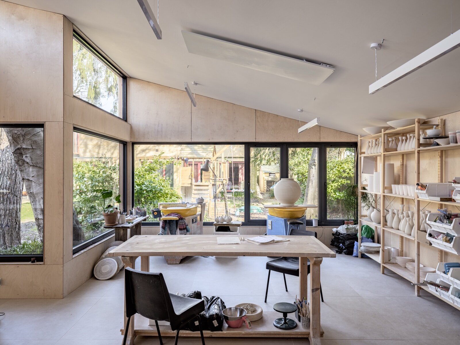 Interior of a garden building fitted out as a pottery studio, with wheels, shelving and a work table