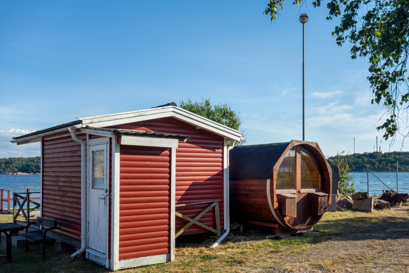 Wooden barrel sauna and a red timber changing cabin beside water