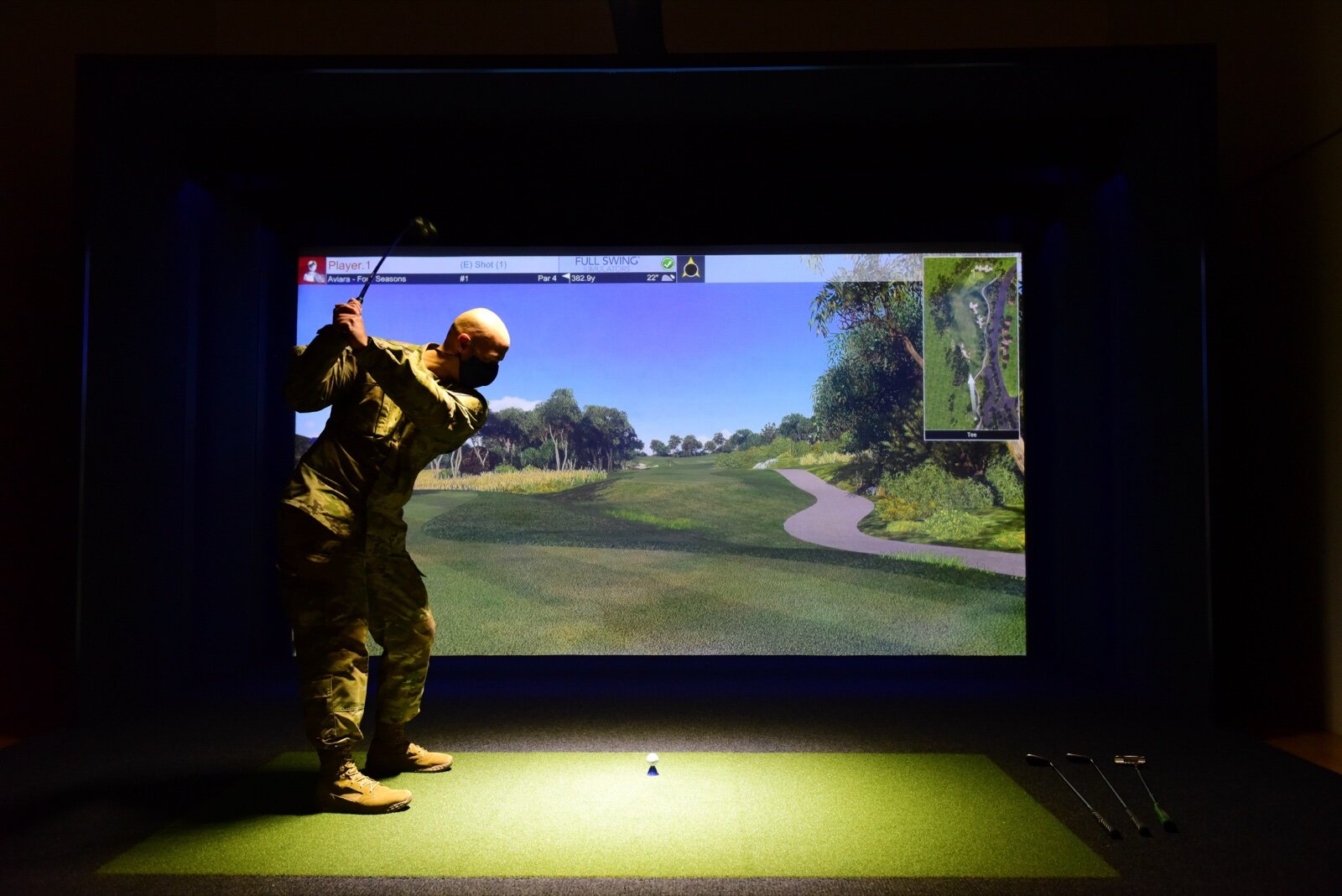 A golfer at the top of the backswing in front of a lit indoor golf simulator impact screen