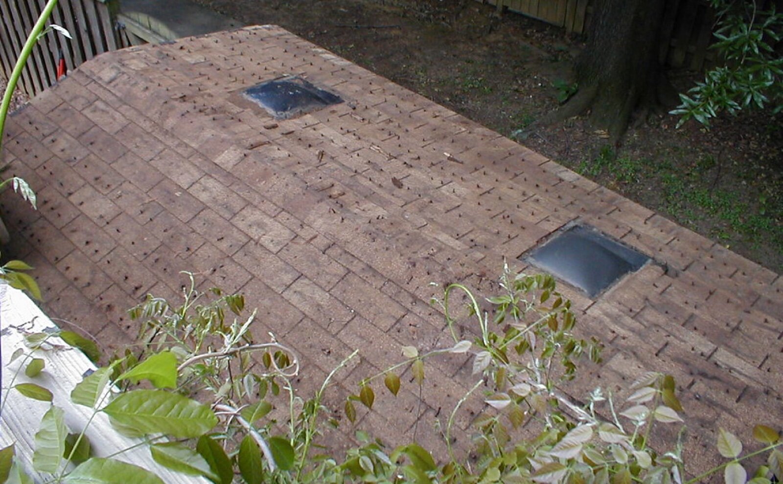 Worn brown felt shingle shed roof with two domed rooflights and nail heads showing across the courses