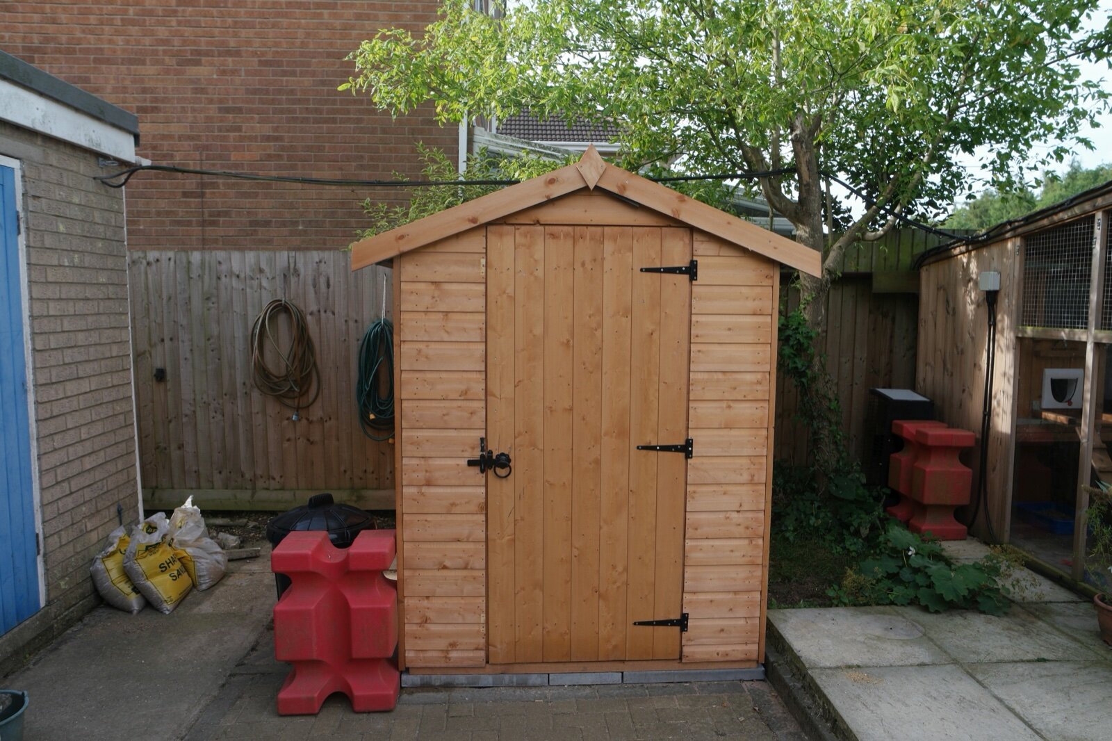 A small new apex wooden shed with a single door standing on a patio