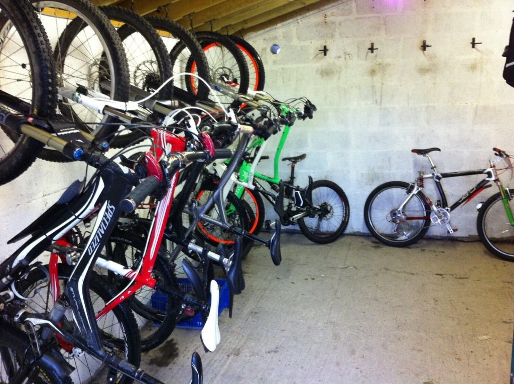 Bicycles hung on wall hooks and standing on the floor inside a whitewashed bike shed