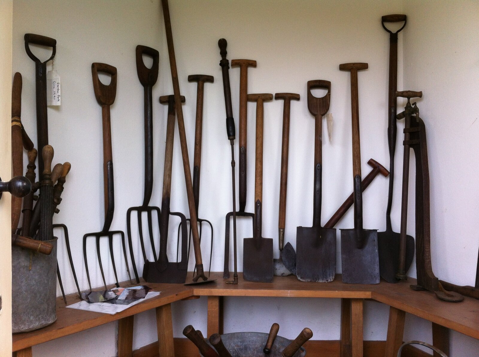 Spades, forks and rakes stored upright against a wall above a wooden bench