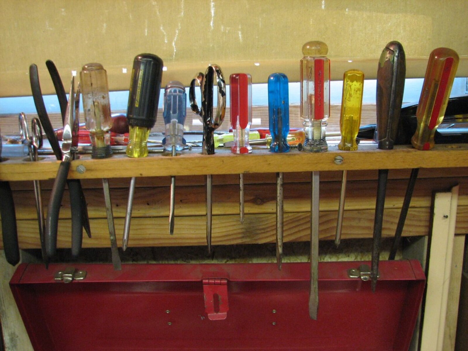 Screwdrivers and pliers held upright in a timber rack along the back of a workbench