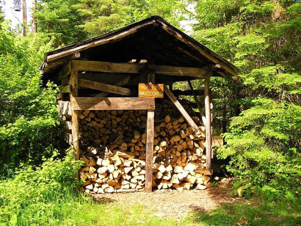 Open-fronted timber woodshed with split logs stacked under a pitched roof